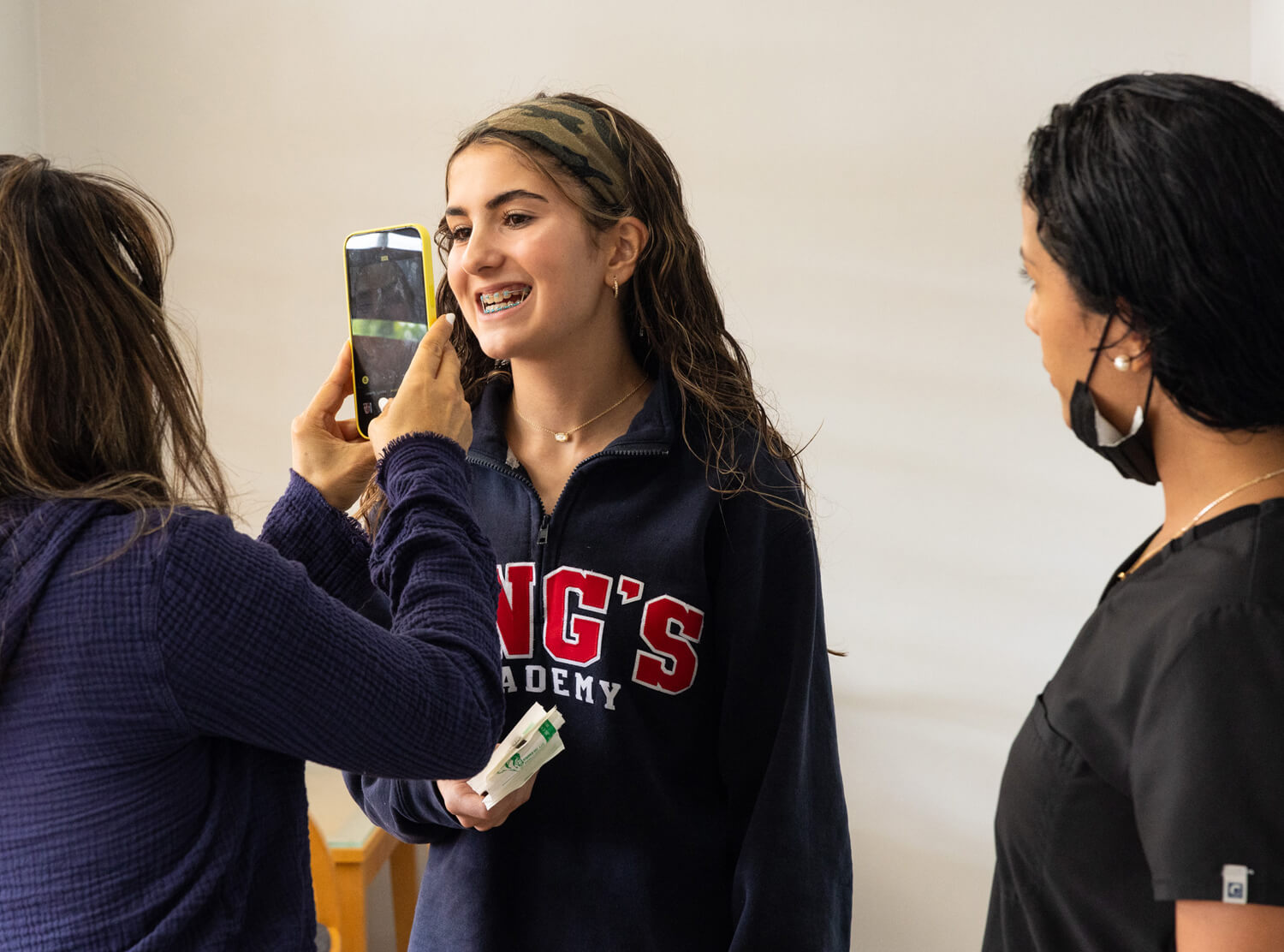 Three people smiling while one takes a selfie in an orthodontics office setting.