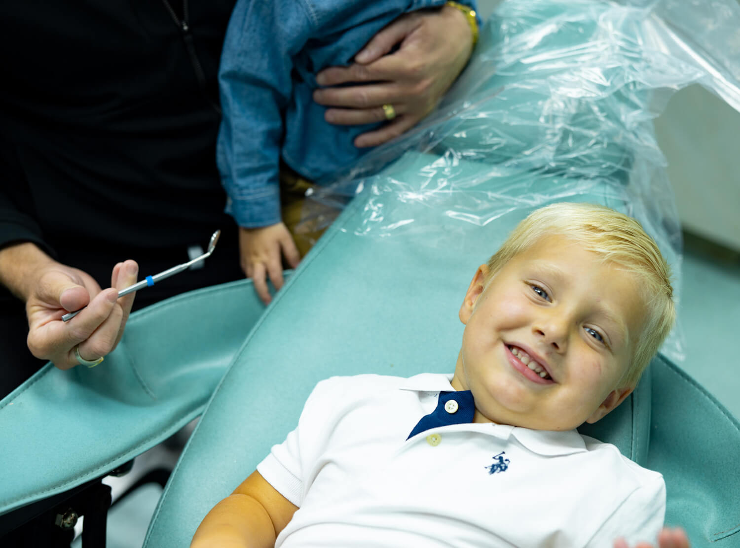 Young child smiling during dental examination in orthodontic office with dentist present.