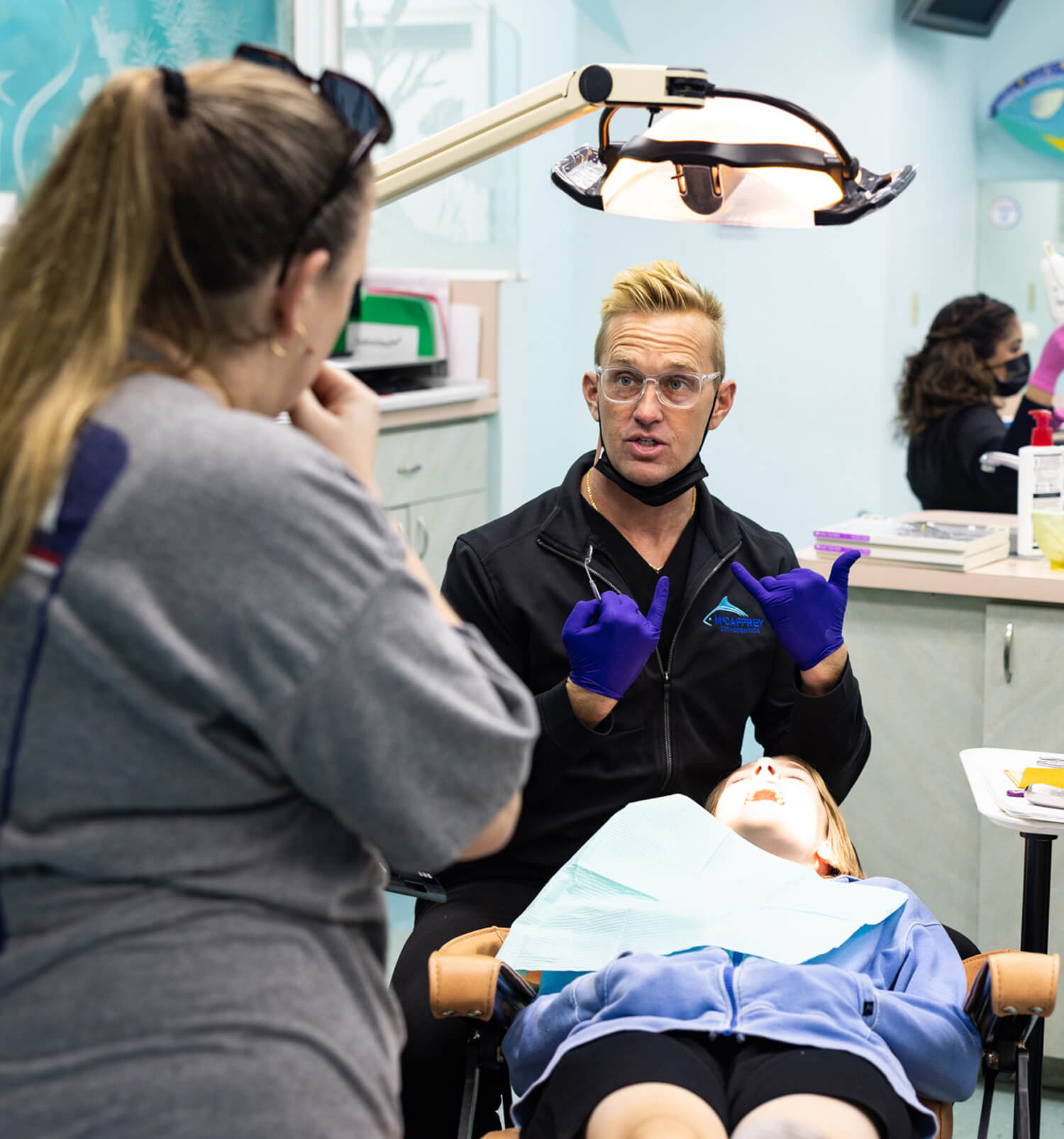 Orthodontist examines patient's teeth during consultation in modern dental office with assistant present.