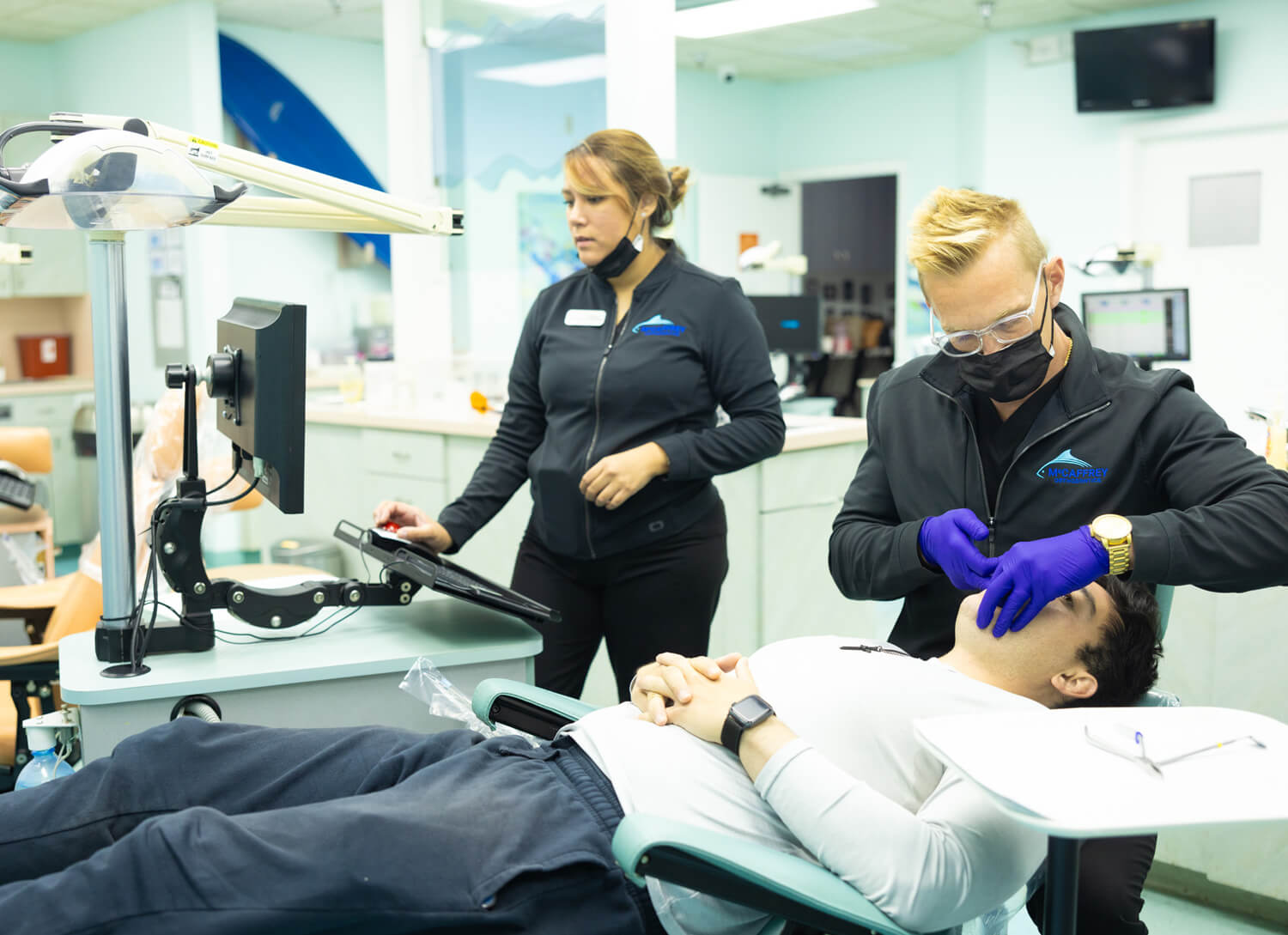 Two dental professionals examine a patient in a modern clinical treatment room.