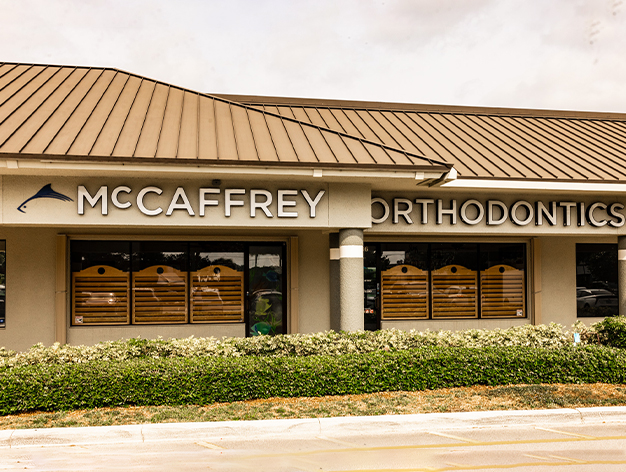 McCaffrey Orthodontics storefront with tan exterior, metal roof, and wooden door panels in a strip mall setting.