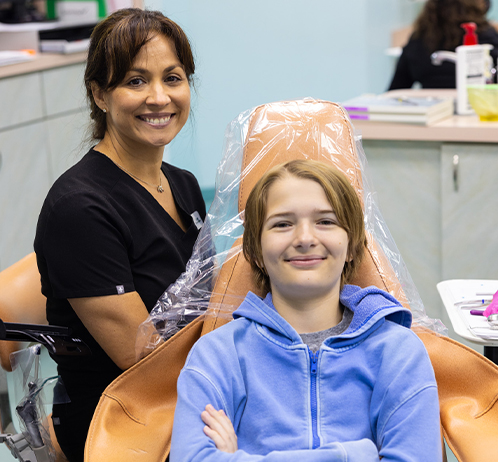 Orthodontist applying plastic wrap to young patient's hair in clinical treatment room.