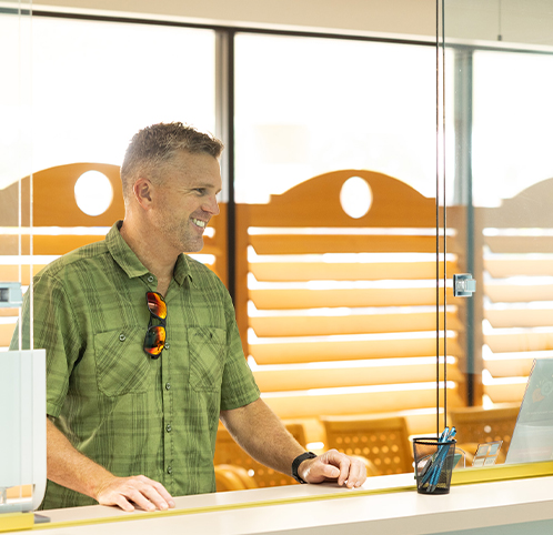 Man in green shirt speaking at orthodontics office counter with modern window blinds