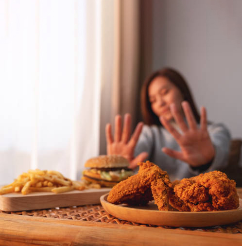 Woman declining fried food, french fries and chicken on table in bright kitchen.