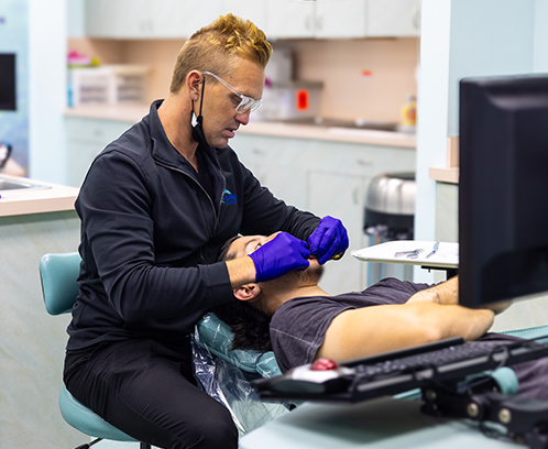 Orthodontist in purple gloves examining patient's teeth in clinical dental office setting.