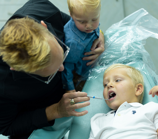 Orthodontist examining young child's teeth during dental appointment with parent present.