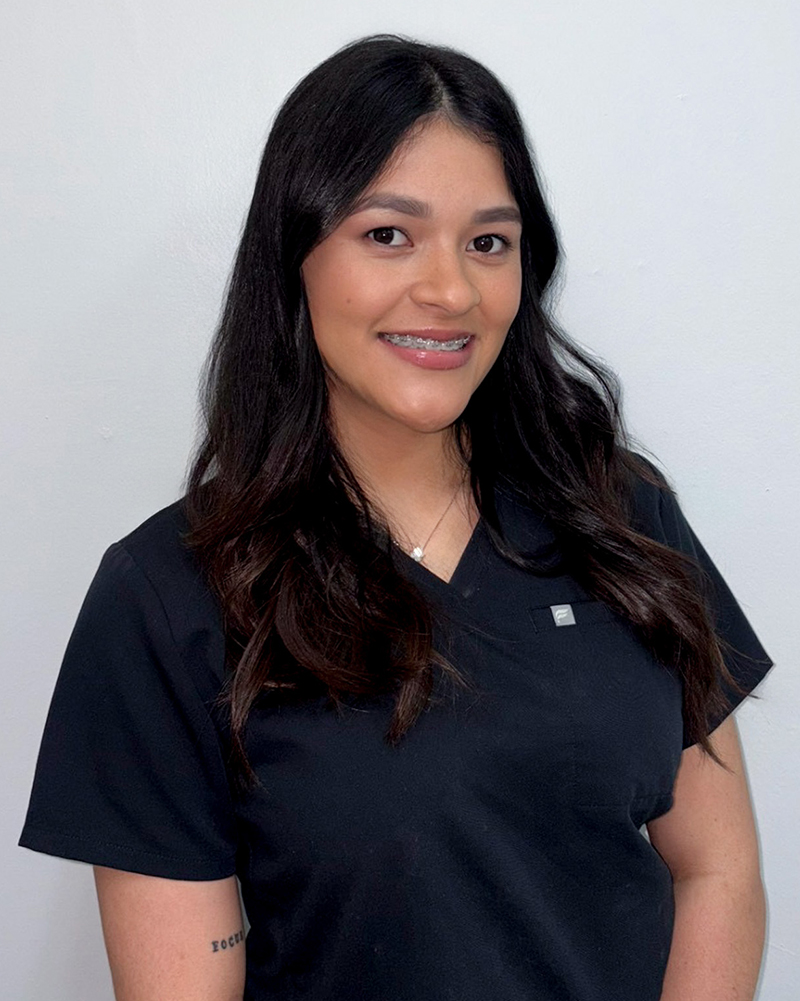 Professional headshot of smiling woman in dark scrubs against white background.